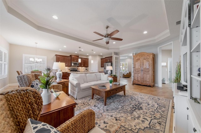 living room featuring plenty of natural light, ceiling fan with notable chandelier, visible vents, and a tray ceiling