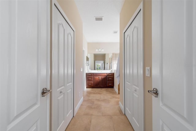 hall featuring a sink, visible vents, baseboards, and light tile patterned floors