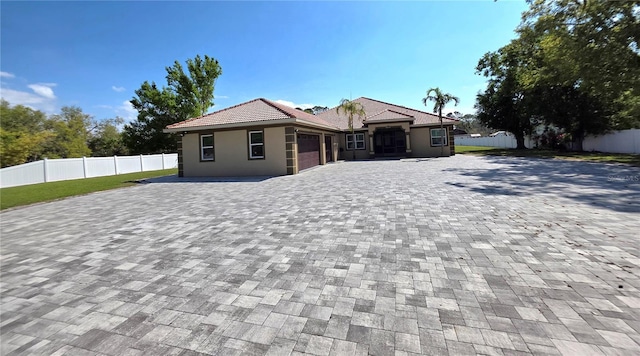 view of front of house with a tiled roof, decorative driveway, fence, and an attached garage