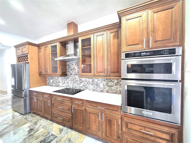 kitchen with tasteful backsplash, appliances with stainless steel finishes, wall chimney exhaust hood, brown cabinetry, and glass insert cabinets