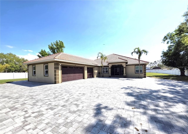 view of front of property with fence, a tiled roof, stucco siding, decorative driveway, and a garage