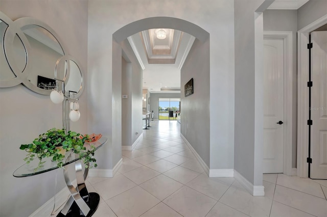 hallway featuring a tray ceiling, light tile patterned flooring, baseboards, and ornamental molding