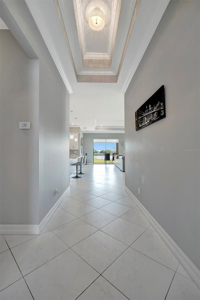 hallway with a raised ceiling, light tile patterned floors, baseboards, and ornamental molding