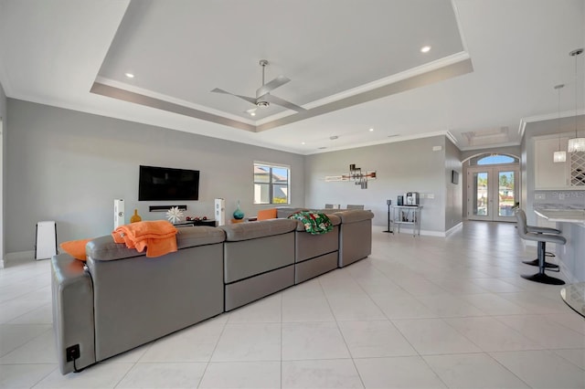 living area featuring baseboards, a tray ceiling, ornamental molding, french doors, and a ceiling fan