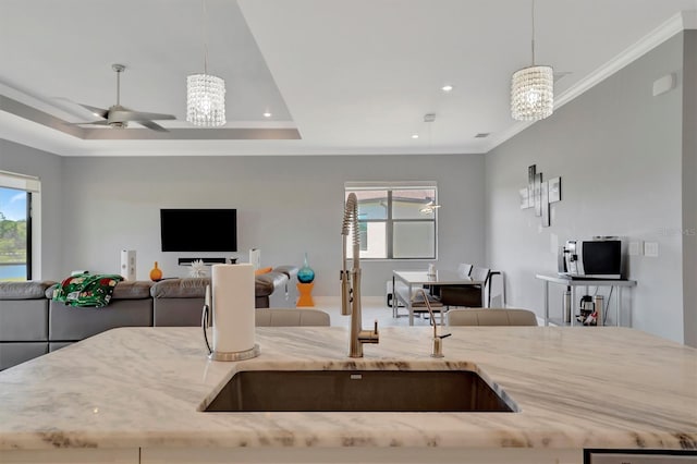 kitchen featuring light stone countertops, a tray ceiling, ornamental molding, a sink, and open floor plan