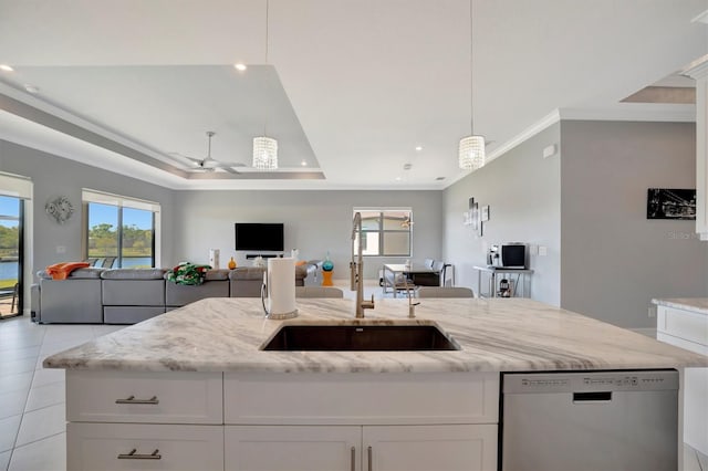 kitchen featuring light stone counters, a sink, stainless steel dishwasher, a raised ceiling, and open floor plan