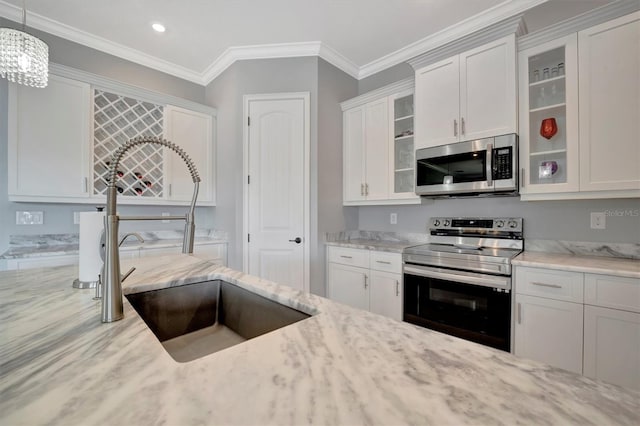 kitchen featuring light stone countertops, ornamental molding, stainless steel appliances, white cabinetry, and a sink