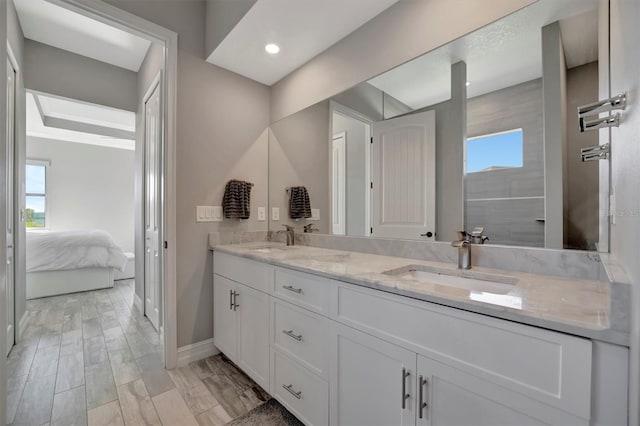 ensuite bathroom with a sink, baseboards, ensuite bath, and double vanity