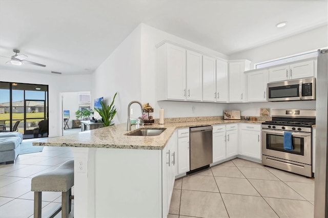 kitchen featuring open floor plan, light tile patterned floors, appliances with stainless steel finishes, a peninsula, and a sink