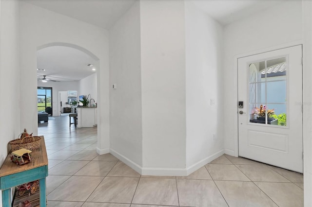 foyer entrance featuring ceiling fan, baseboards, arched walkways, and light tile patterned flooring