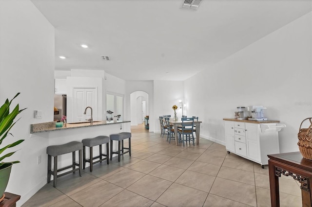 kitchen with visible vents, a breakfast bar, freestanding refrigerator, white cabinetry, and arched walkways