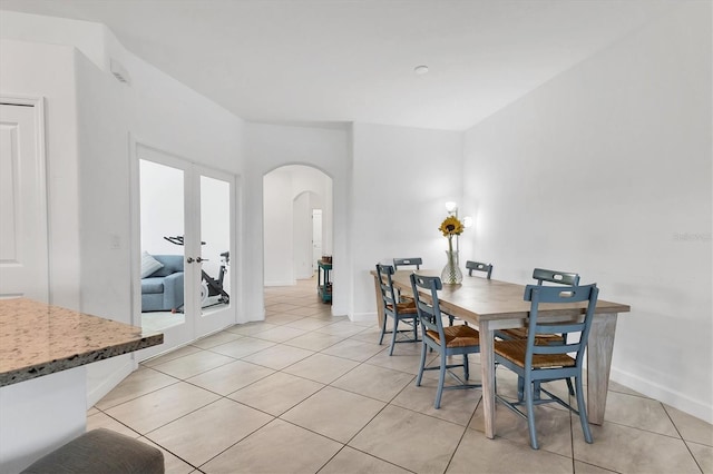 dining space featuring light tile patterned floors, french doors, arched walkways, and baseboards