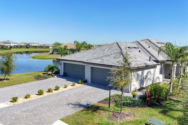 view of front facade featuring a garage, decorative driveway, stucco siding, and a water view