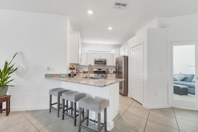 kitchen with visible vents, a peninsula, a sink, appliances with stainless steel finishes, and a kitchen bar