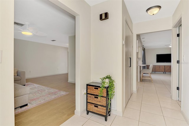 hallway featuring visible vents, baseboards, and light wood finished floors