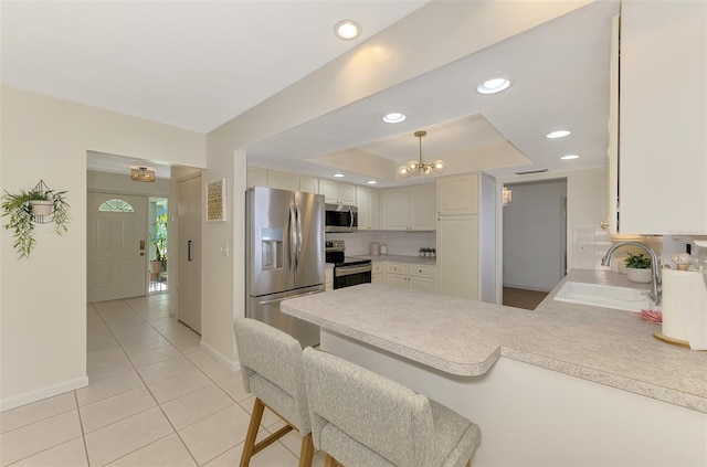 kitchen featuring a peninsula, a tray ceiling, recessed lighting, a sink, and appliances with stainless steel finishes