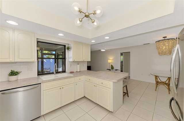 kitchen with backsplash, appliances with stainless steel finishes, a peninsula, an inviting chandelier, and a sink