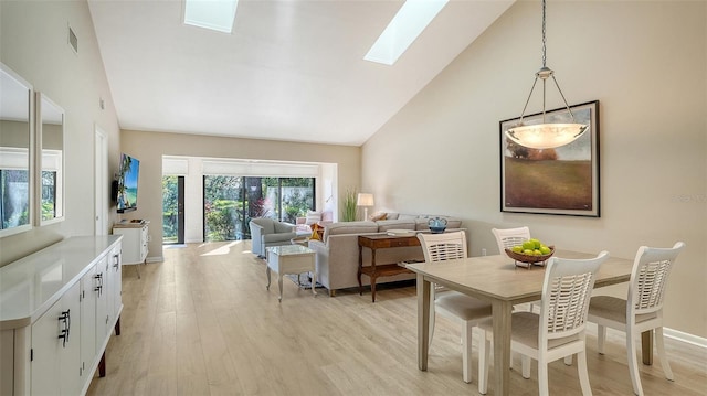 dining room with light wood finished floors, high vaulted ceiling, a skylight, and visible vents