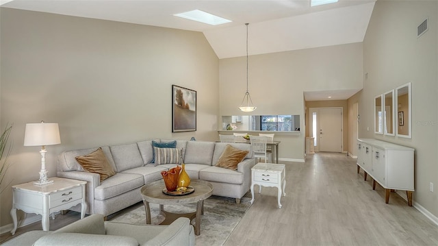 living room with visible vents, high vaulted ceiling, light wood-style flooring, a skylight, and baseboards