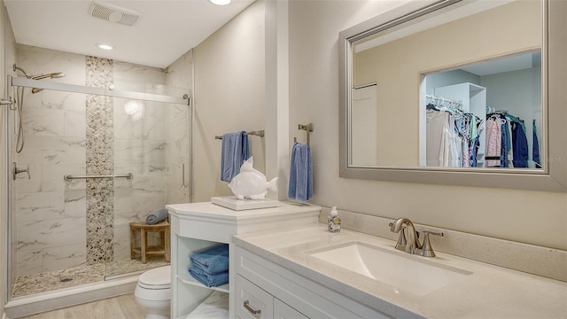 full bathroom featuring vanity, visible vents, a shower stall, a walk in closet, and toilet