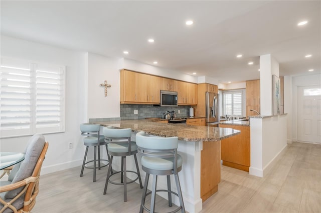 kitchen featuring a kitchen breakfast bar, appliances with stainless steel finishes, a peninsula, decorative backsplash, and light stone countertops