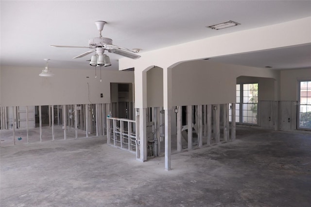 empty room with visible vents, arched walkways, concrete floors, and ceiling fan