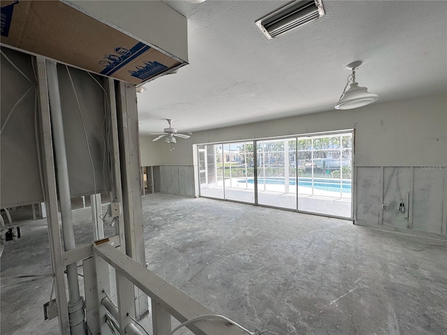 interior space featuring visible vents, a textured ceiling, a ceiling fan, and a wainscoted wall