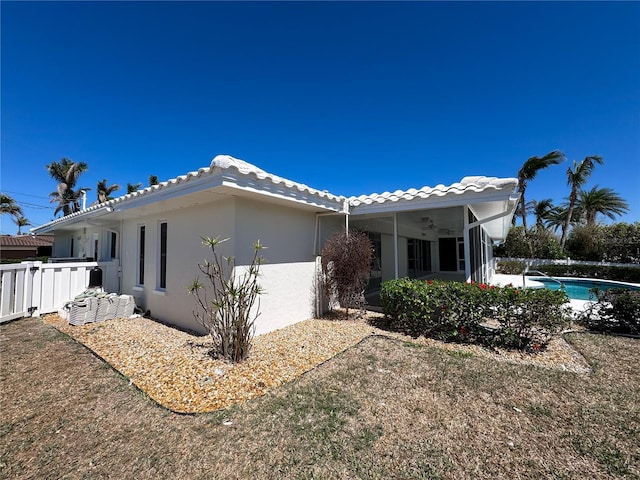 view of side of property with a fenced in pool, fence, a sunroom, stucco siding, and a tiled roof