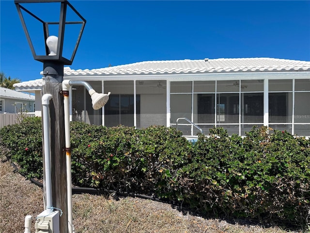 exterior space featuring a sunroom, a ceiling fan, and a tile roof