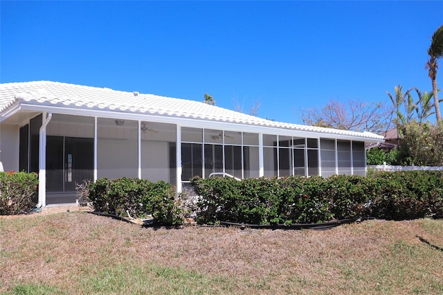 rear view of property featuring a lawn, a tile roof, and a sunroom