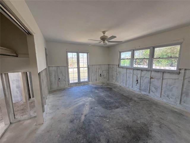 unfurnished room with ceiling fan, unfinished concrete flooring, and wainscoting