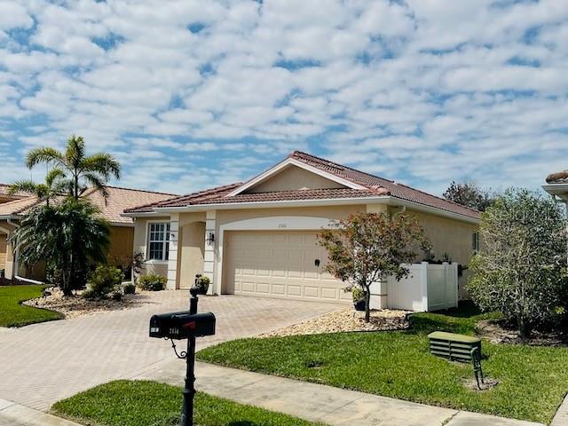 ranch-style house featuring a front yard, fence, stucco siding, a garage, and decorative driveway