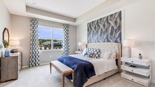 bedroom with a tray ceiling, light colored carpet, and baseboards