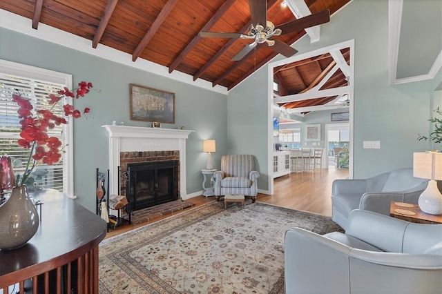 living room featuring a ceiling fan, wood finished floors, lofted ceiling with beams, wooden ceiling, and a brick fireplace