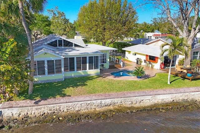 back of house with a yard, a deck with water view, a sunroom, and a chimney