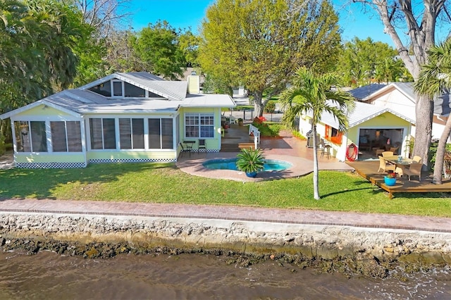 rear view of house with a deck with water view, a lawn, a sunroom, and a chimney