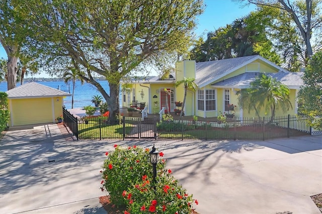 view of front facade with a fenced front yard, a water view, a chimney, and driveway