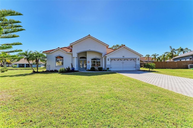 mediterranean / spanish house with stucco siding, a tile roof, decorative driveway, fence, and an attached garage