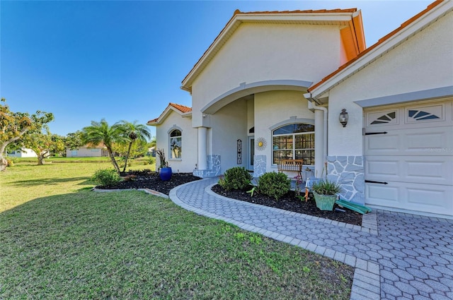 entrance to property featuring a tile roof, a yard, a garage, and stucco siding