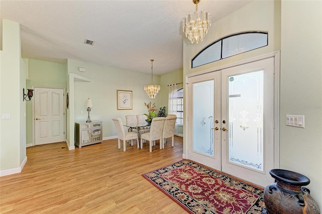 foyer with a chandelier, visible vents, french doors, and light wood-style floors