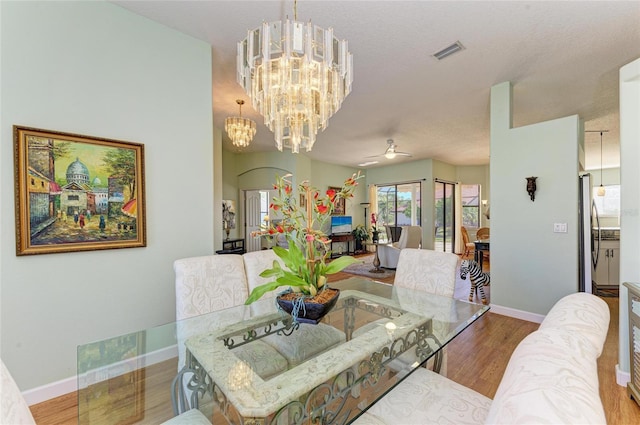 dining space featuring visible vents, baseboards, wood finished floors, and ceiling fan with notable chandelier