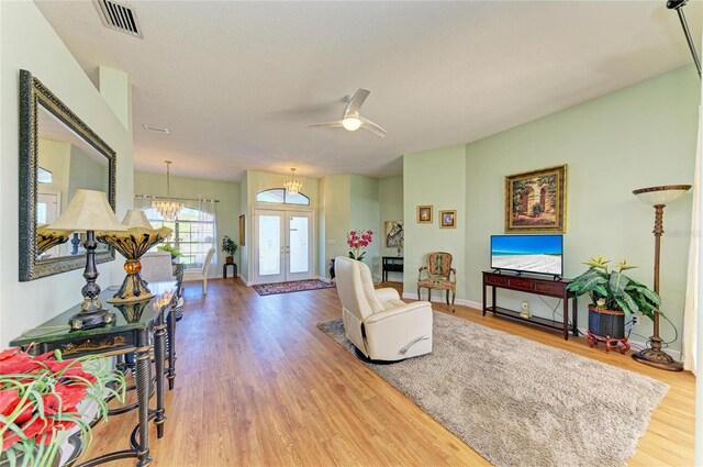 living area with visible vents, ceiling fan with notable chandelier, wood finished floors, french doors, and baseboards