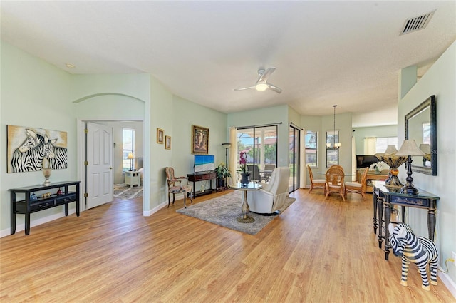 living area featuring visible vents, ceiling fan with notable chandelier, baseboards, and light wood-style floors