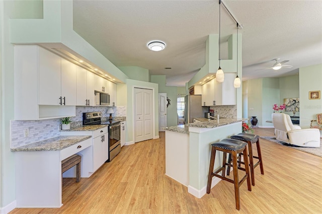 kitchen with a breakfast bar area, light wood-style flooring, appliances with stainless steel finishes, a peninsula, and white cabinetry