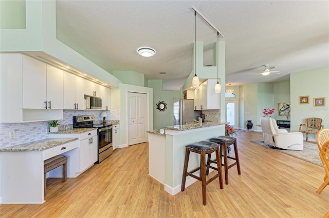 kitchen featuring light stone counters, appliances with stainless steel finishes, a kitchen breakfast bar, light wood-style floors, and white cabinets