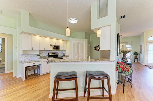 kitchen with visible vents, decorative backsplash, appliances with stainless steel finishes, a kitchen breakfast bar, and light wood-type flooring