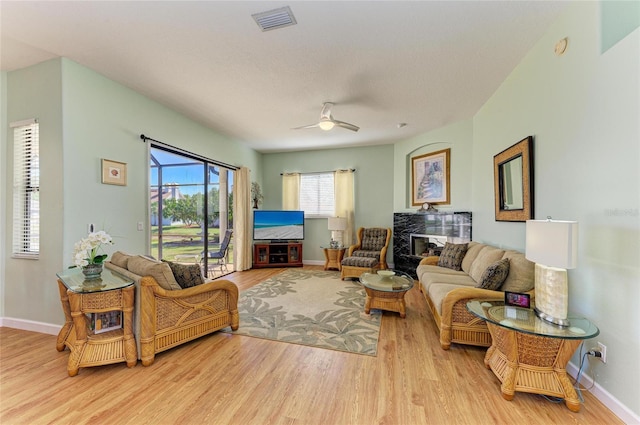 living area with wood finished floors, visible vents, baseboards, a fireplace, and ceiling fan