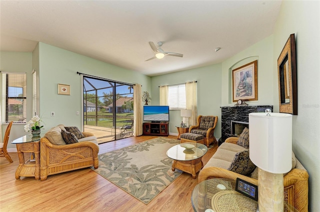 living area with a high end fireplace, baseboards, wood finished floors, and a ceiling fan