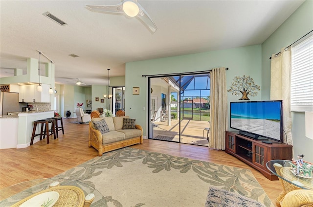 living room featuring light wood finished floors, visible vents, and a ceiling fan