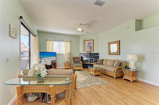 living area featuring wood finished floors, baseboards, visible vents, ceiling fan, and a textured ceiling